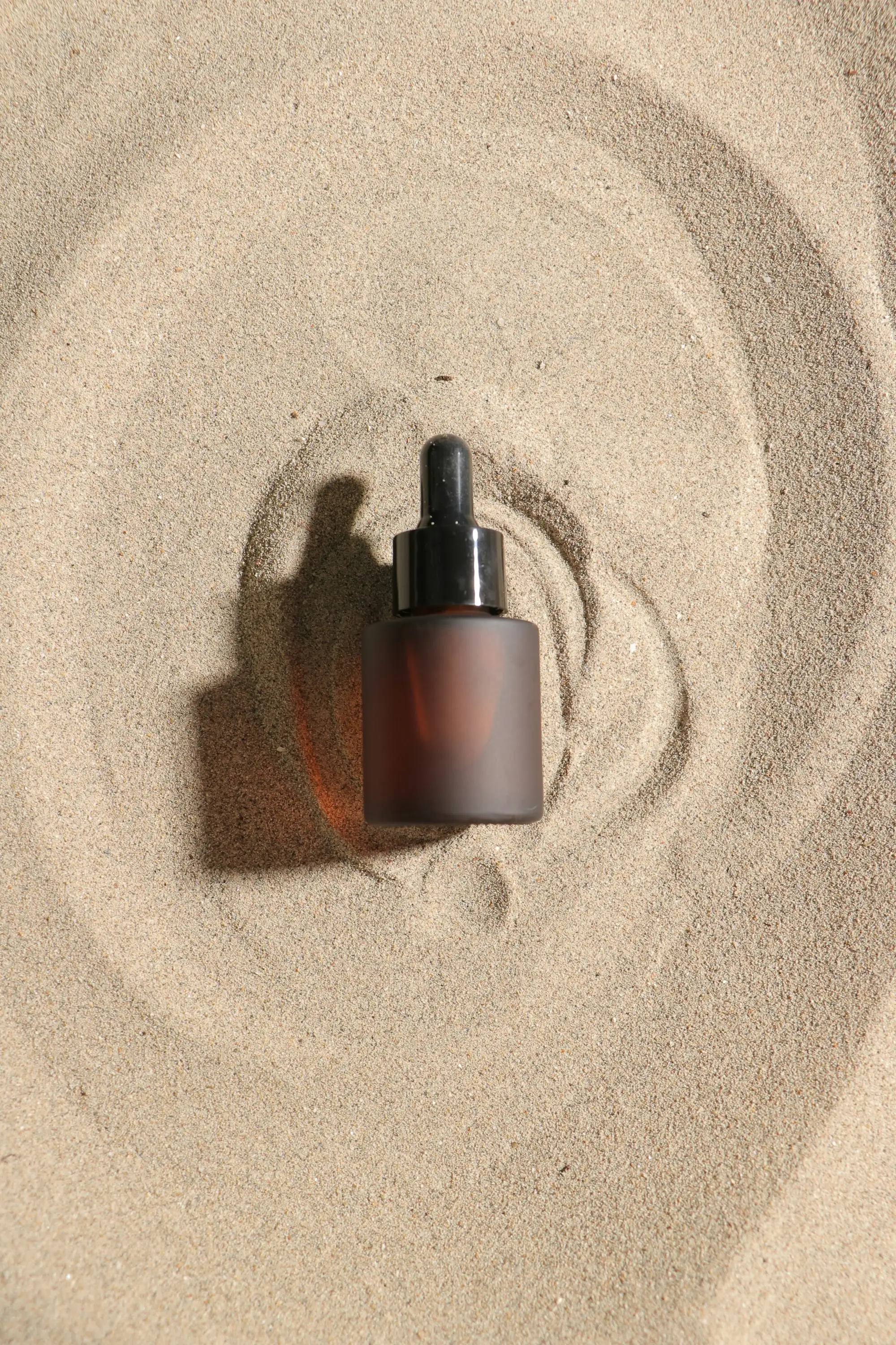 Aralia Solene face oil, a frosted amber bottle resting in raked sand