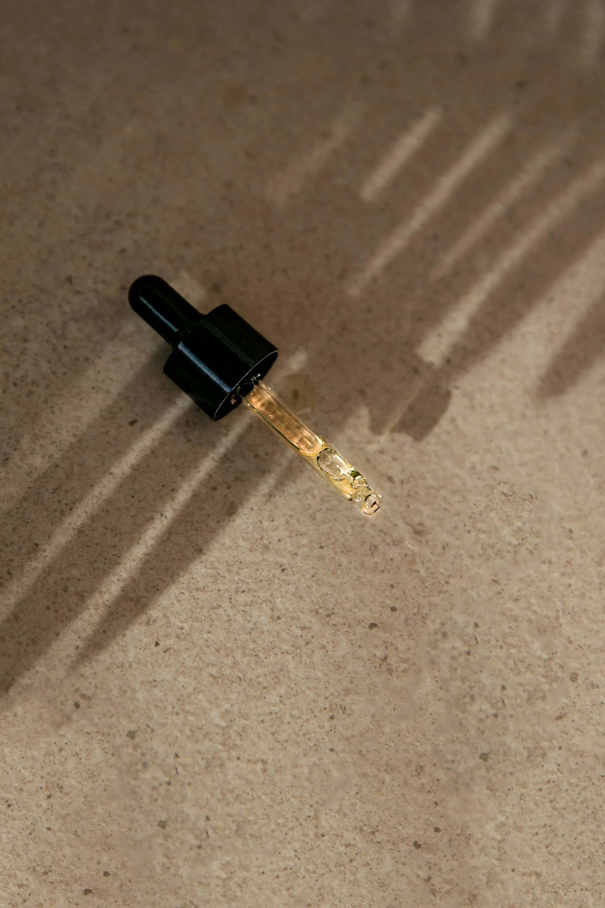 An amber dropper casting a louvred shadow across warm sand